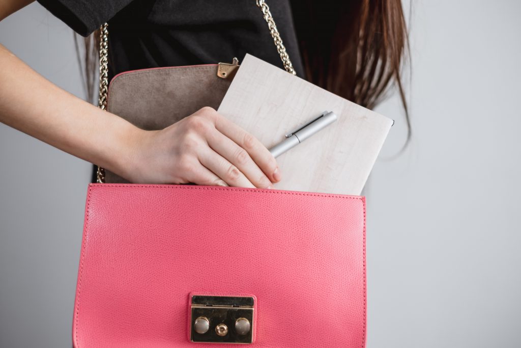 女性がピンク色のバッグにペンとノートを入れようとしている
