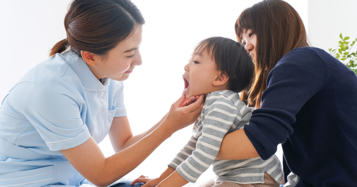 母親に抱えられ歯医者で歯を見せている子供