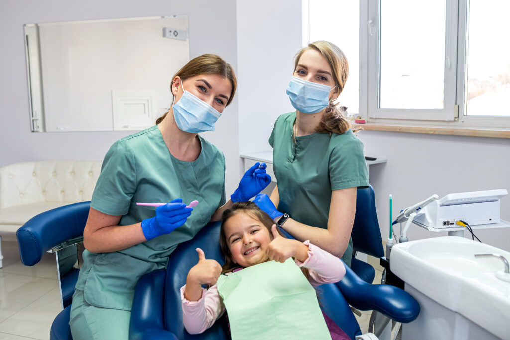 歯科医院の中で笑顔でポーズをしている女の子と女医2人